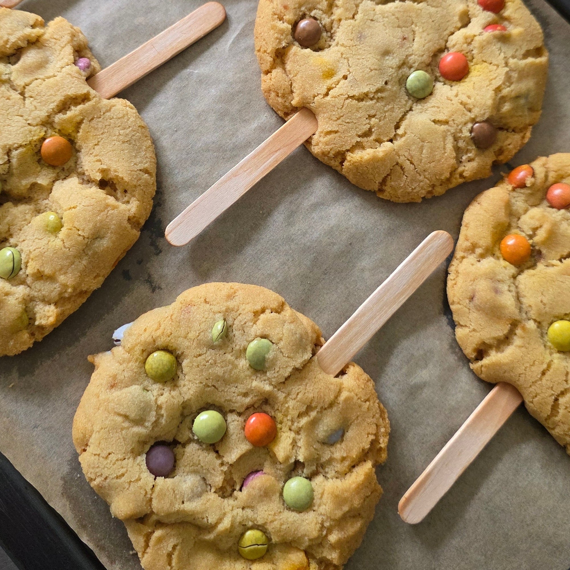 Bake With Rana Crunchy Cookie Pops with colourful chocolate beans on sticks arranged on a baking tray.